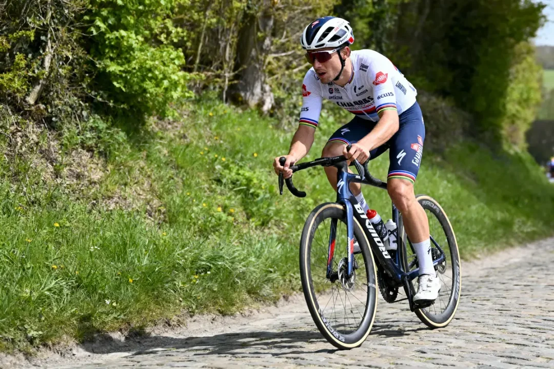 Cycliste en maillot blanc sur route pavée, entouré de verdure.