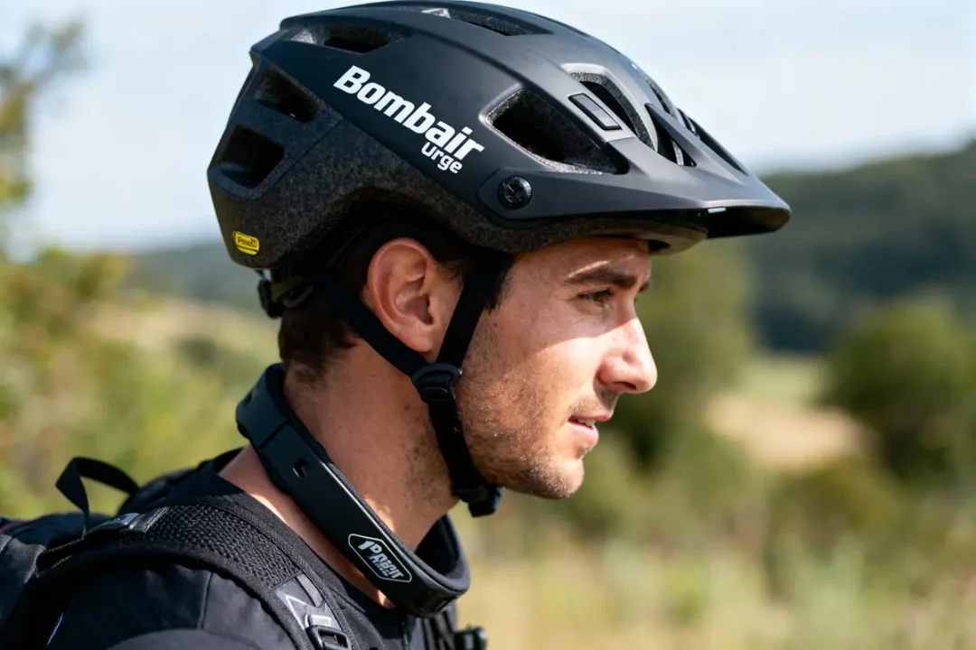 Homme avec casque de vélo noir, profil, arrière-plan flou naturel, portant un collier de protection.