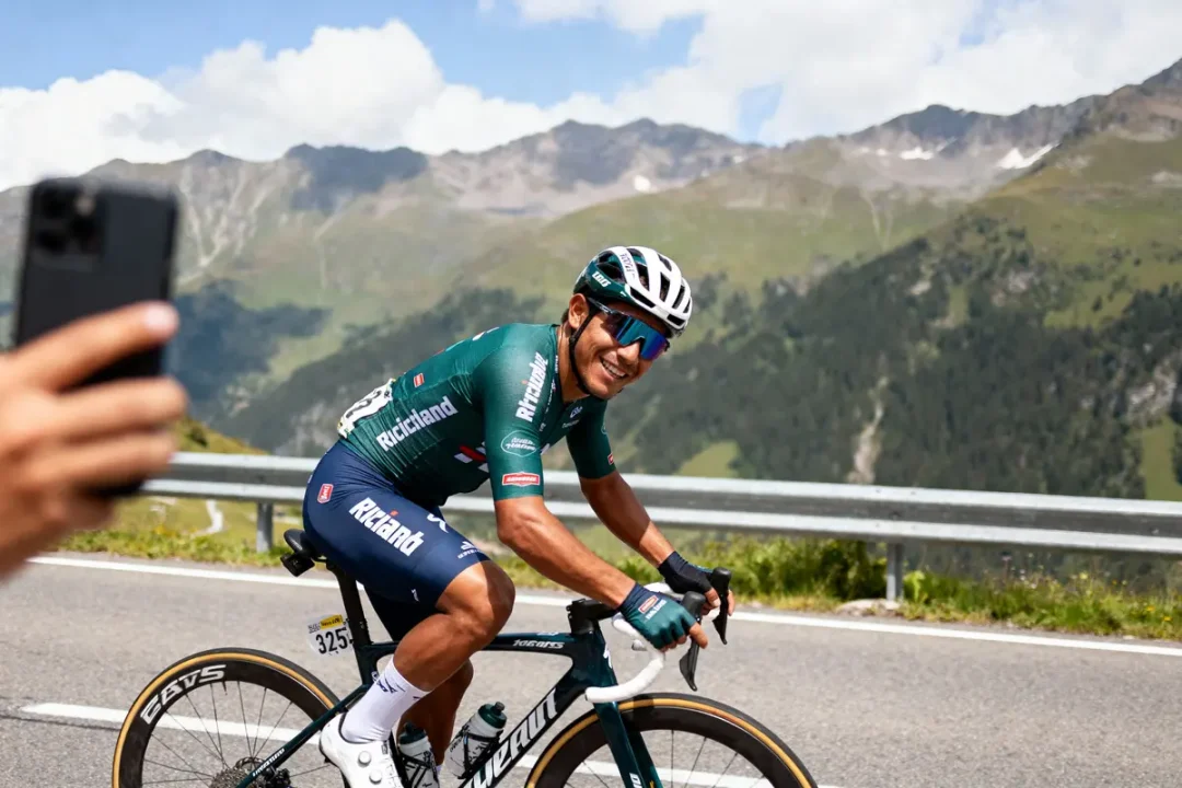 Cycliste souriant en tenue verte sur une route de montagne, un photographe en premier plan.