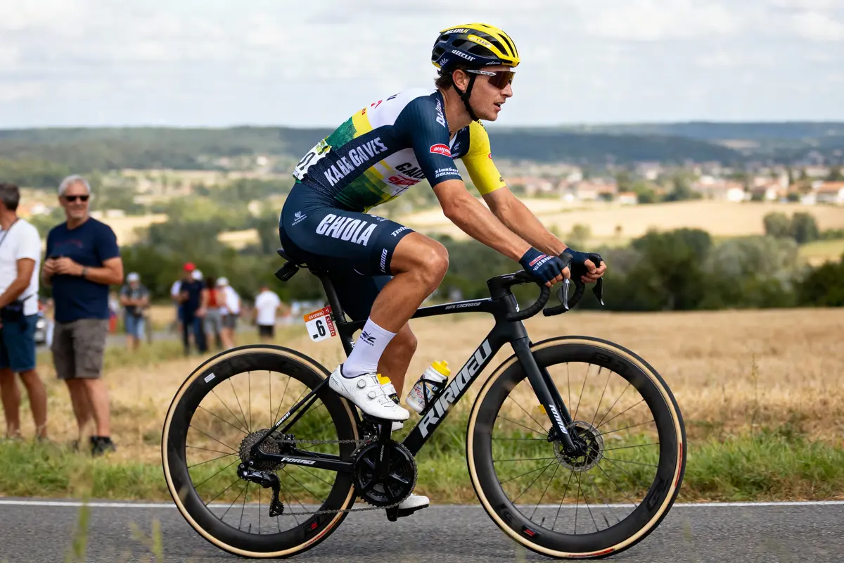 Cycliste en maillot multicolore sur vélo, course en campagne, spectateurs en arrière-plan.
