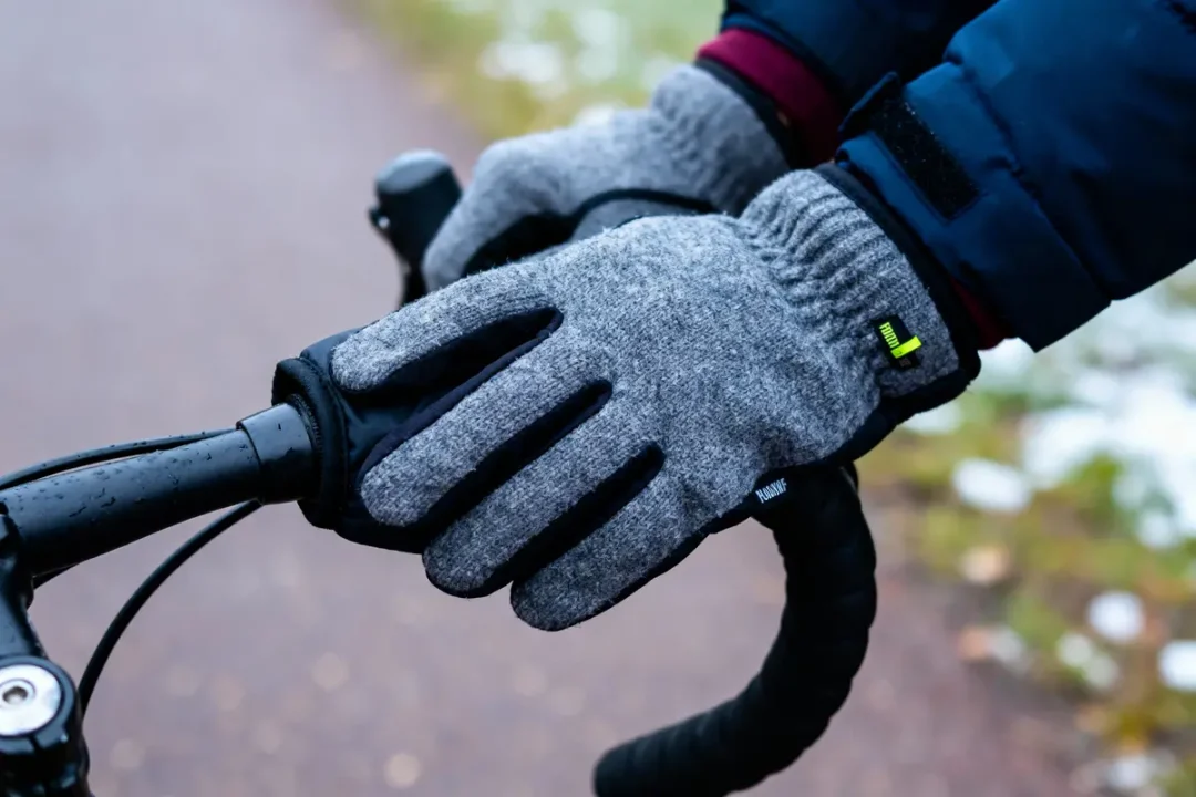 Gants gris sur guidon de vélo par temps froid, personne en veste bleue.