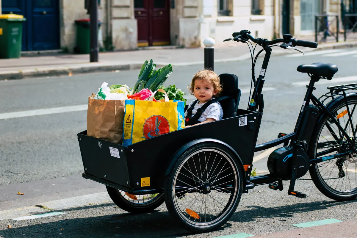 Enfant assis dans un vélo cargo avec sacs de courses sur une rue.