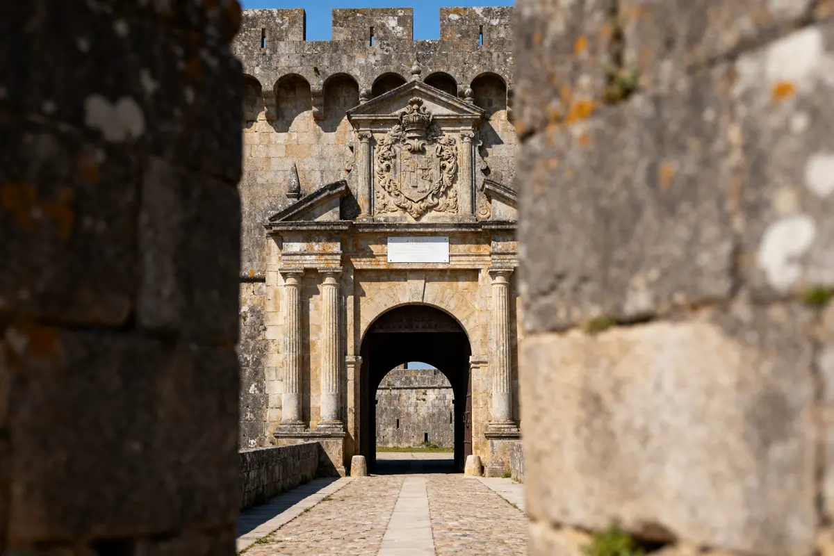 Entrée de forteresse médiévale en pierre avec blason sculpté, vue à travers un passage encadré.