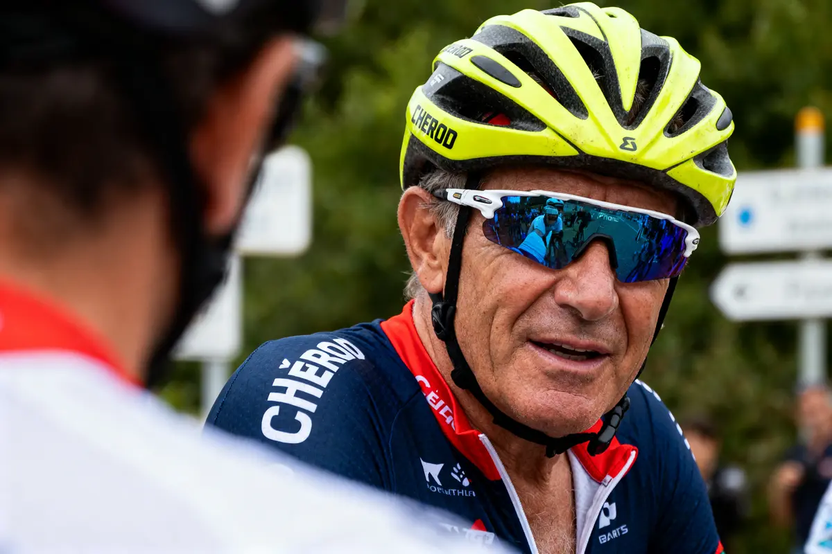 Cycliste portant casque jaune et lunettes bleues, discutant avec un autre cycliste en arrière-plan flou.
