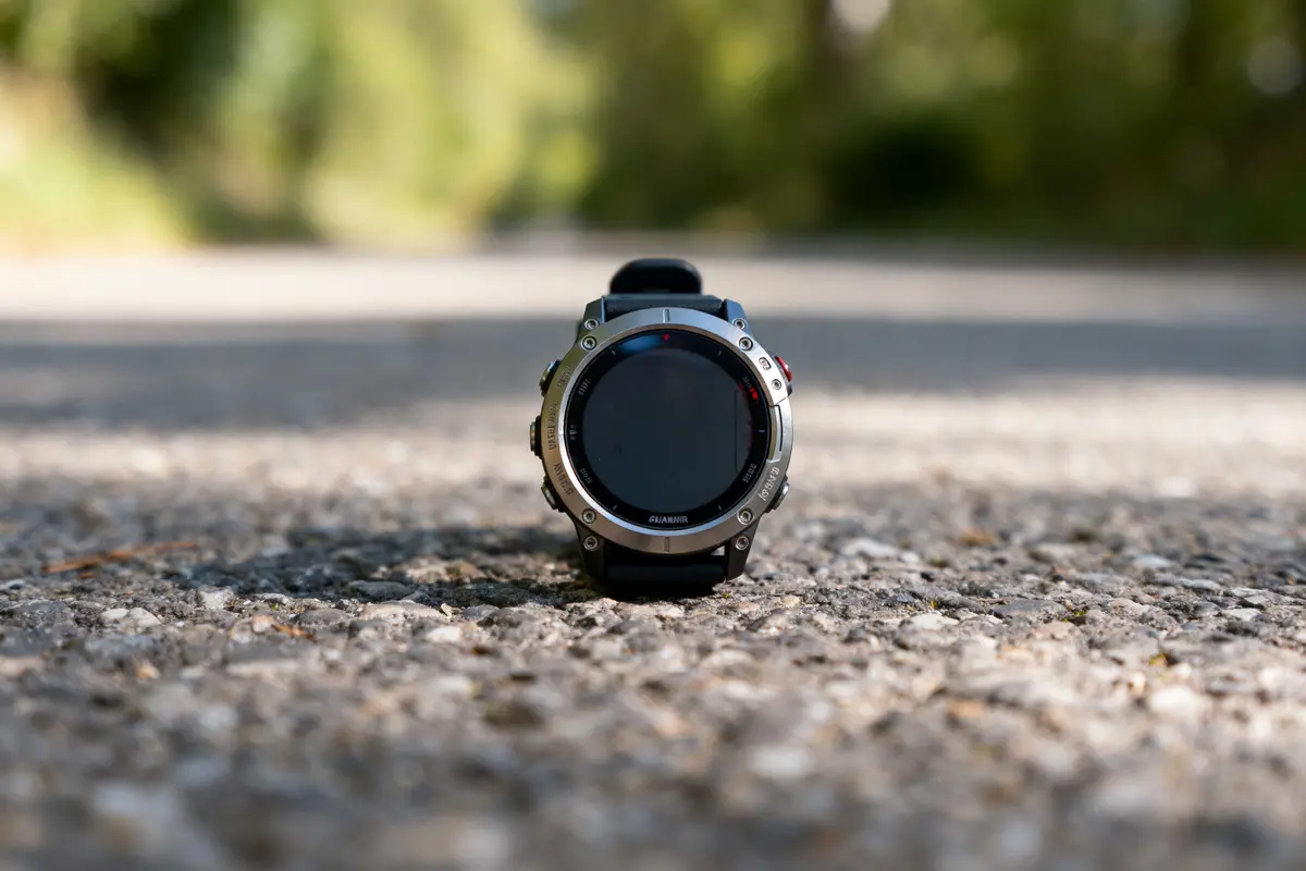 Montre connectée posée sur une route en plein air, avec arrière-plan flou verdoyant.