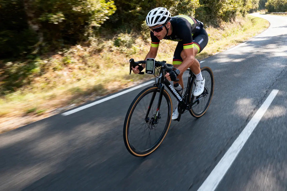 Cycliste en tenue noire, roulant à grande vitesse sur une route bordée d'arbres, casque blanc.