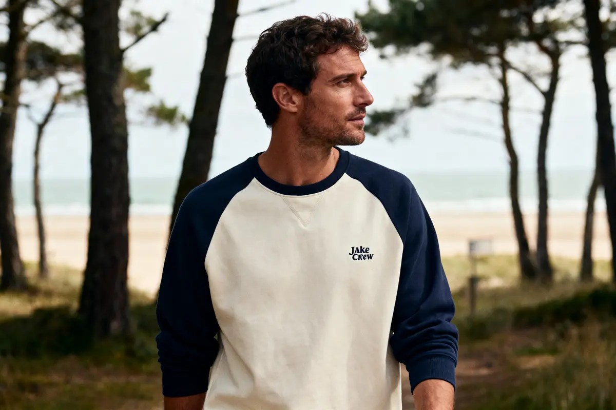 Homme portant un sweat Jake Crew, debout en forĂȘt prĂšs de la plage.