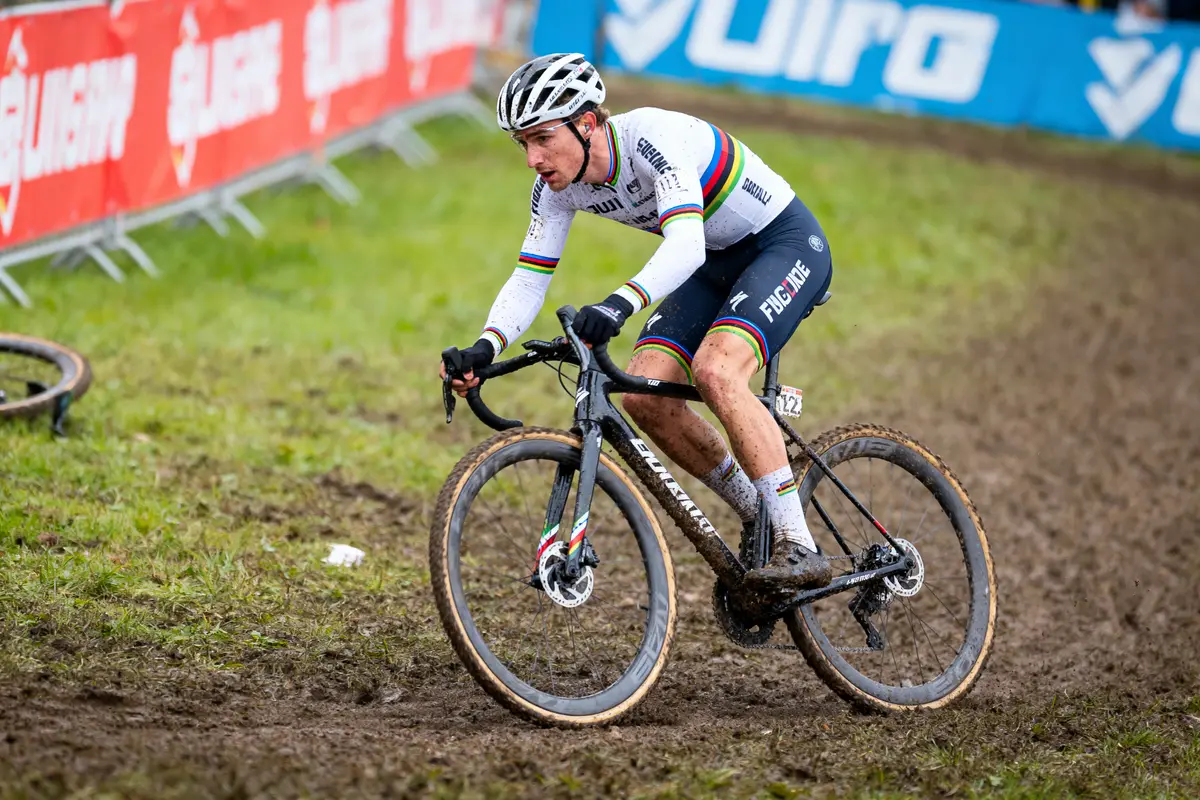 Cycliste en pleine course sur un terrain boueux, vêtu d'une tenue multicolore, casque et vélo noir.