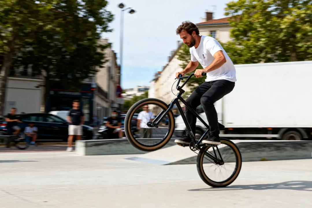 Personne effectuant une figure de BMX sur une roue dans un espace urbain, spectateurs en arrière-plan.