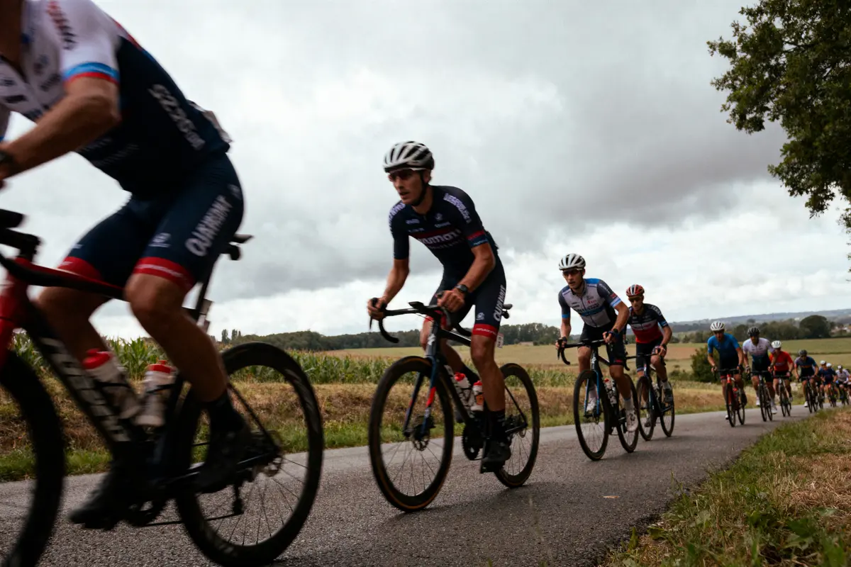 Cyclistes en compétition sur une route de campagne, ciel nuageux, arbres en arrière-plan.