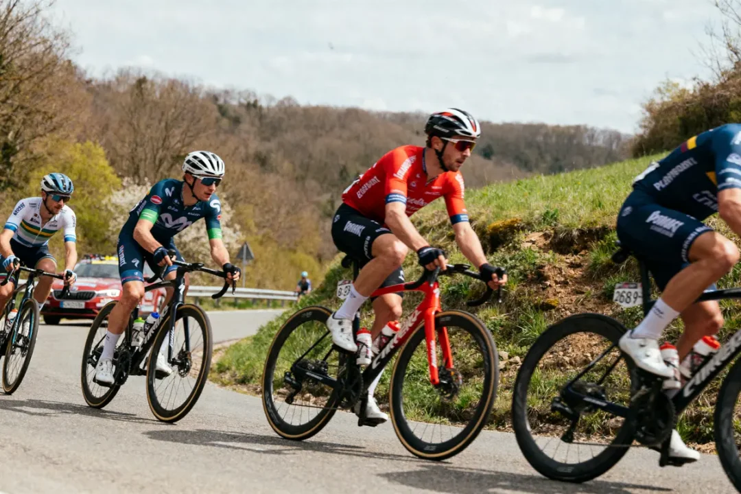 Cyclistes en course sur route sinueuse, entourés de verdure et de voitures suiveuses.