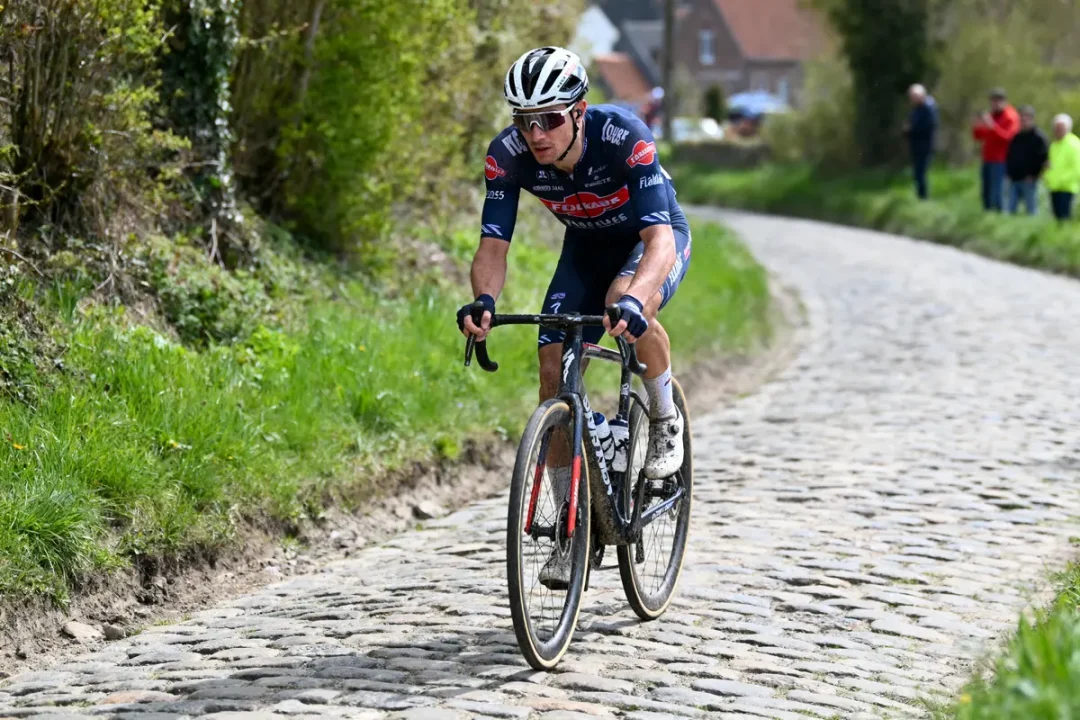 Cycliste en uniforme bleu roulant sur une route pavée en campagne, entouré de verdure.