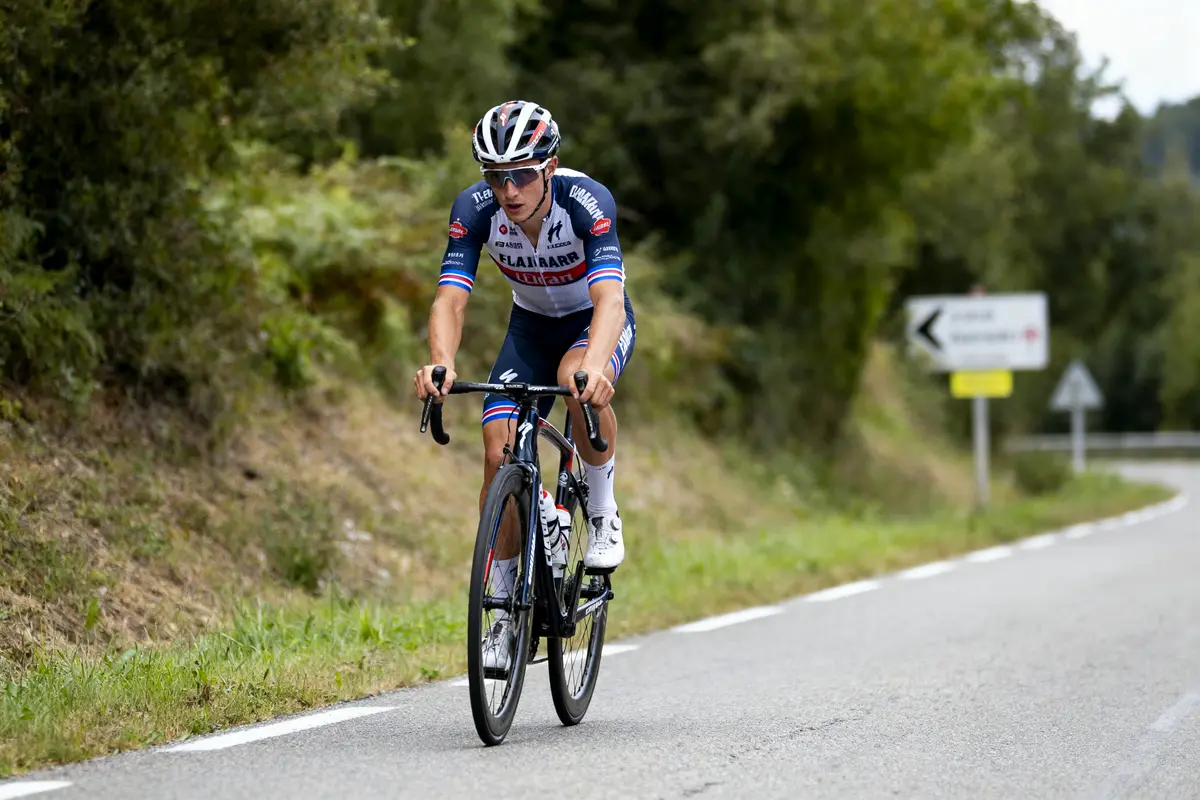 Cycliste sur route bordée de végétation, portant un maillot bleu et blanc, pédale concentré.