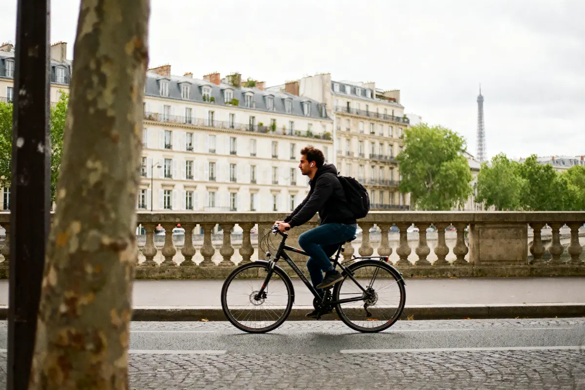 Homme à vélo sur un pont parisien, bâtiments résidentiels et tour Eiffel en arrière-plan.