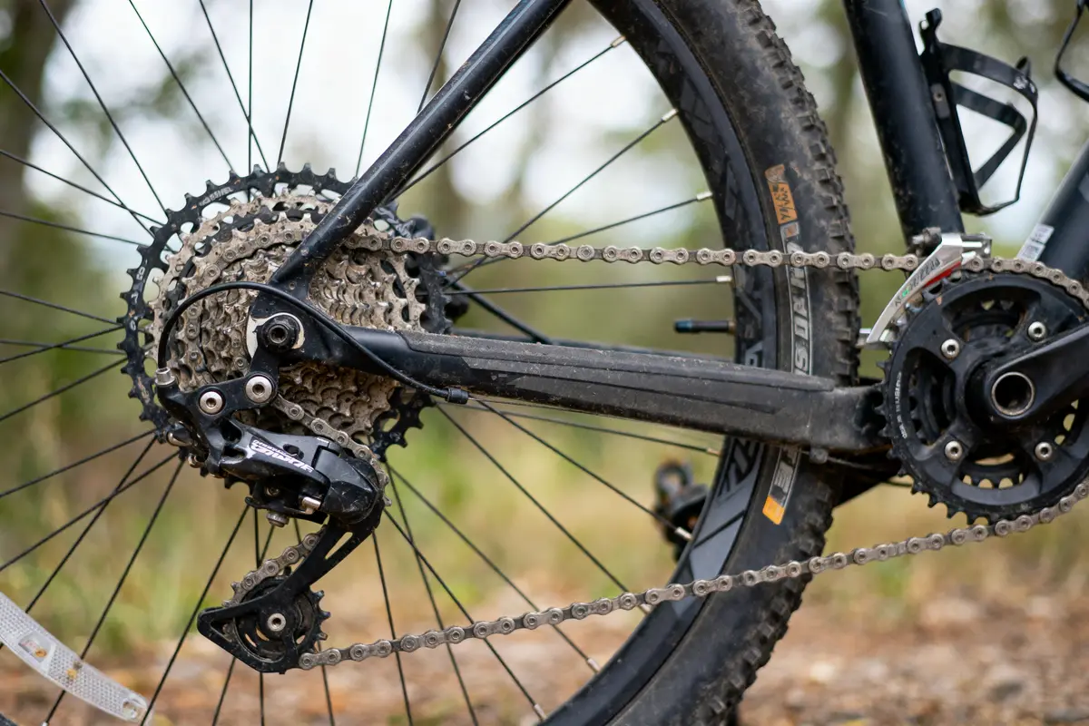 Gros plan d'un dérailleur et roue arrière de vélo de montagne sur fond flou.