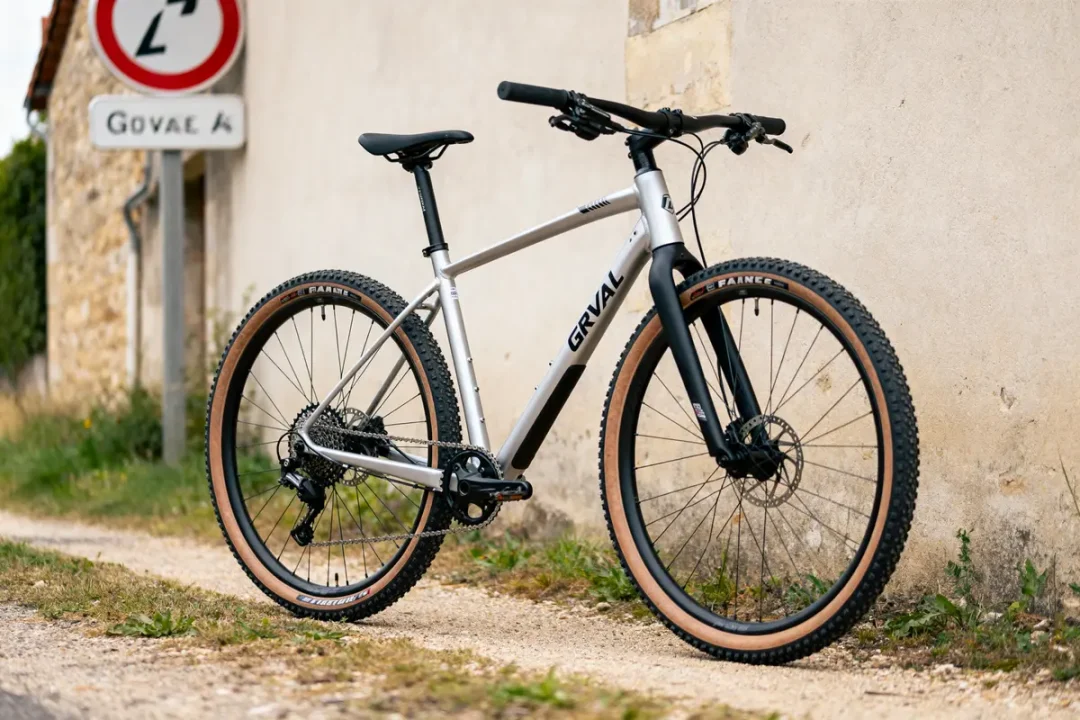 Vélo GRVL argenté sur chemin de terre près d'un mur et panneau de signalisation