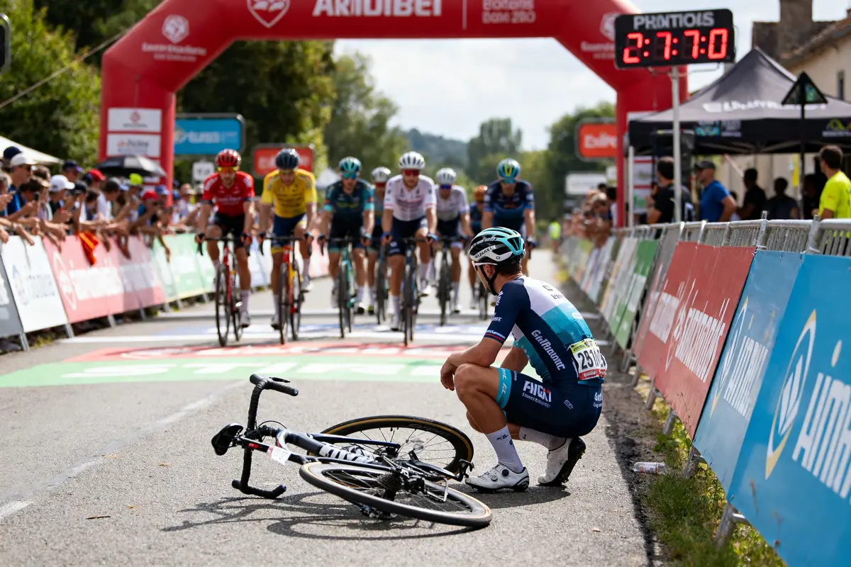 Cycliste assis après chute observant resultat cyclisme avec peloton en arrière-plan franchissant la ligne