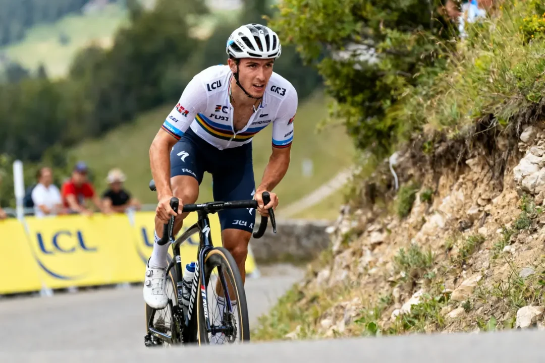 Cycliste en montée lors d'une compétition, Felix Gall portant un maillot blanc racing.