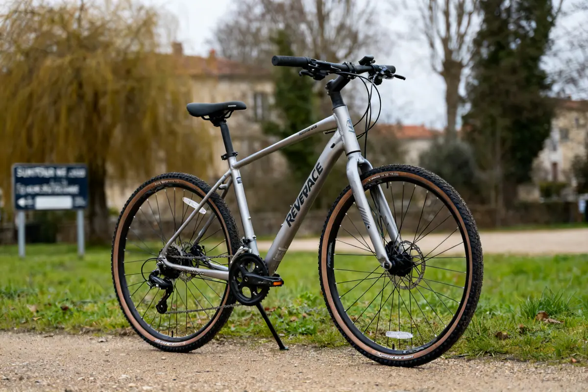 Vélo gris Riverside 700 stationné sur un chemin dans un parc verdoyant.