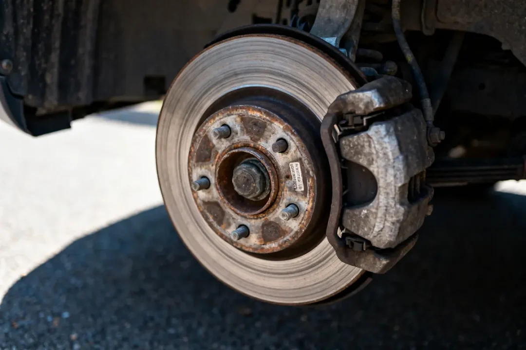 Gros plan sur un disque de frein usé avec étrier rouillé monté sur voiture.
