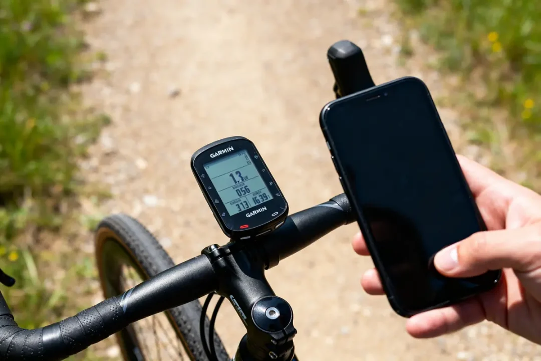 Compteur Garmin Edge installé sur guidon de vélo, écran de smartphone en main.